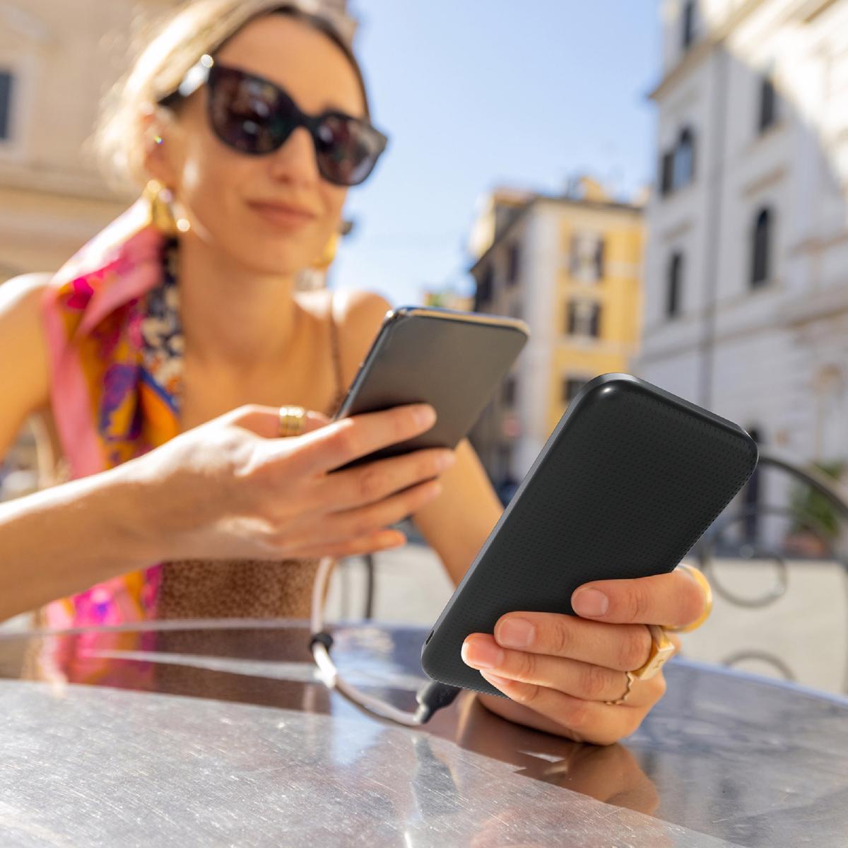 Woman charging phone with a power bank while sitting at cafe outdoors. Concept of charging gadgets for travel